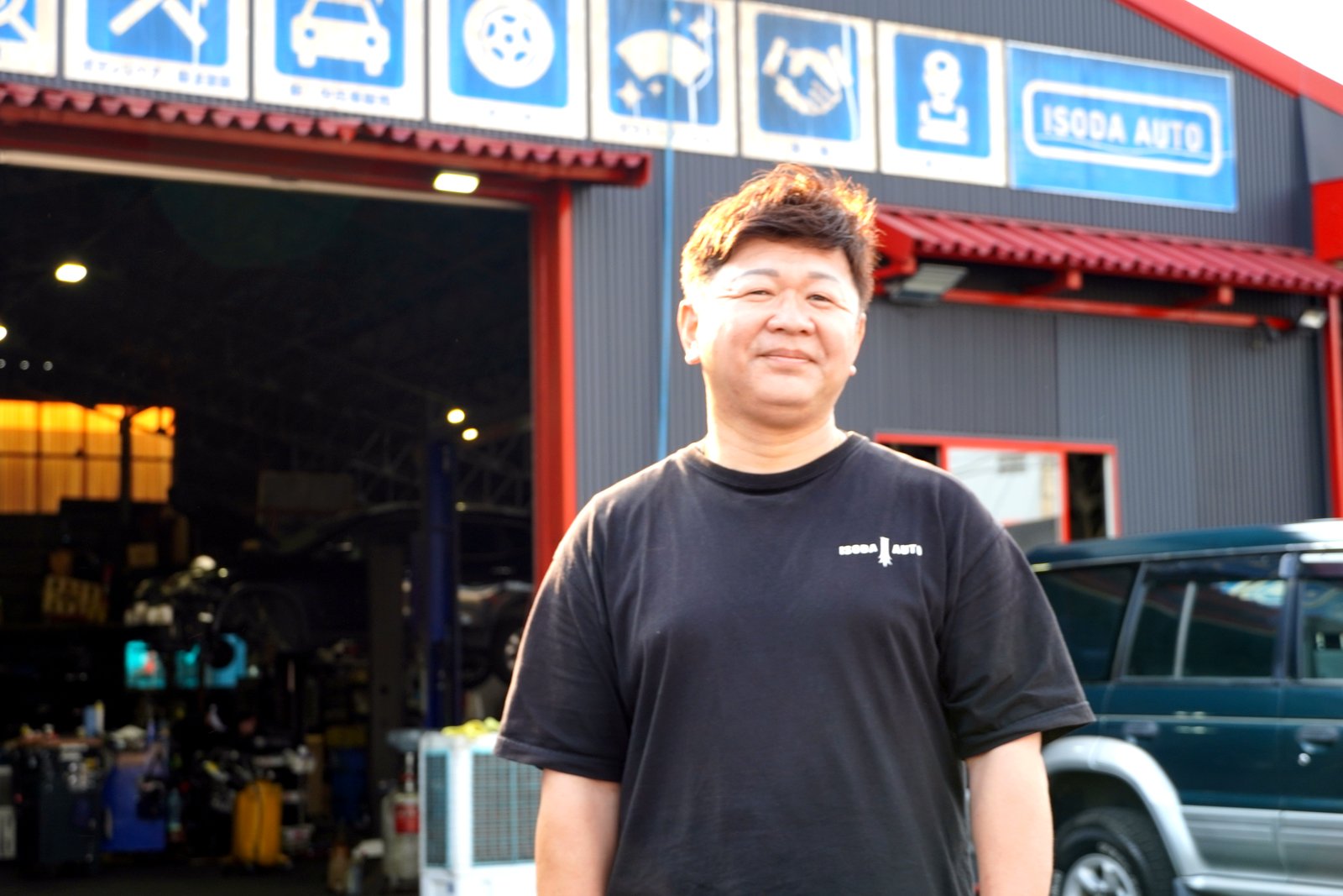 ISODA AUTOの店舗外観に立つ登坂耕也代表