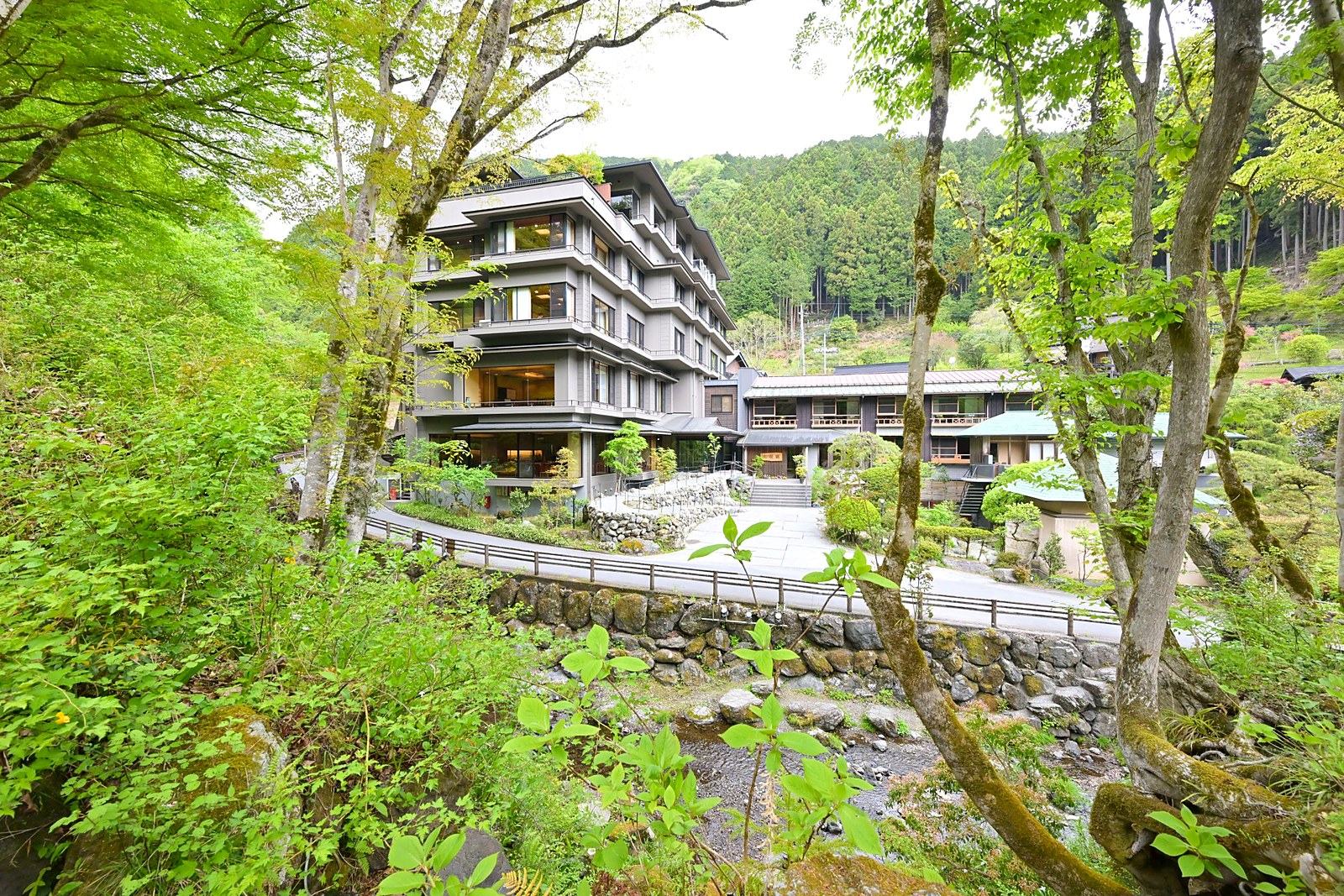 山の稜線を越えないよう5階建てに抑えられた、新緑に包まれる名栗温泉・大松閣の外観