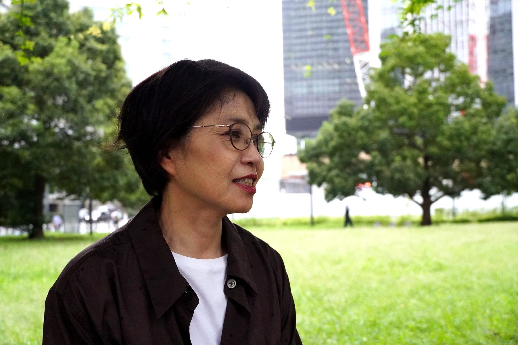 公園の木々を背景に、中国出張での経験を振り返りながら語る三浦さん
