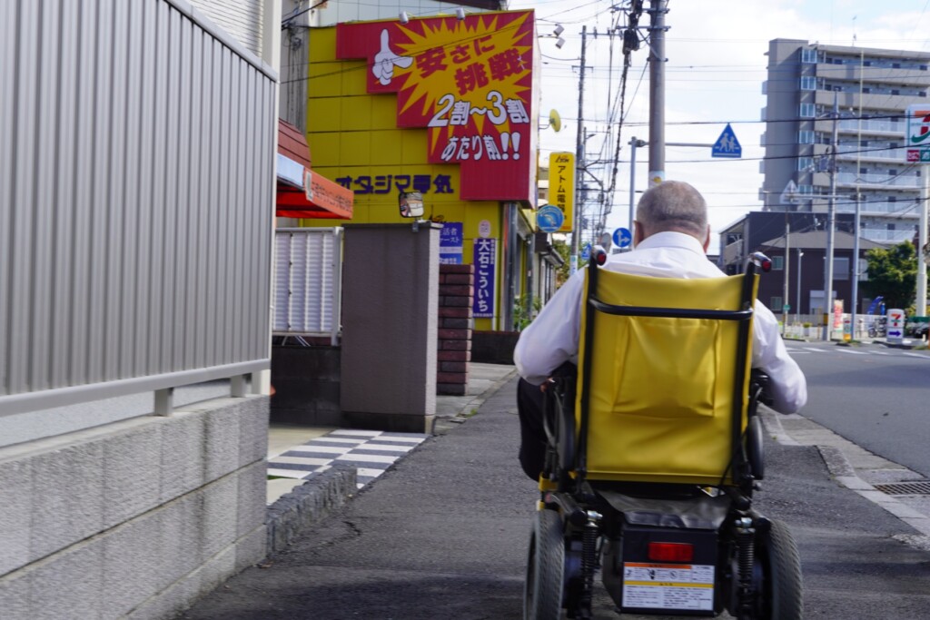 蕨の街を電動車椅子で進む岡崎清春氏の後ろ姿